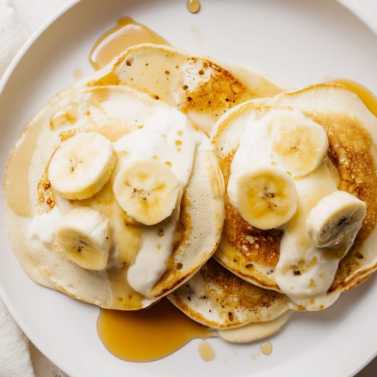 View of fluffy Weekend Golden-Brunch Banana Pancakes with sliced bananas and a sweet maple syrup cascade.