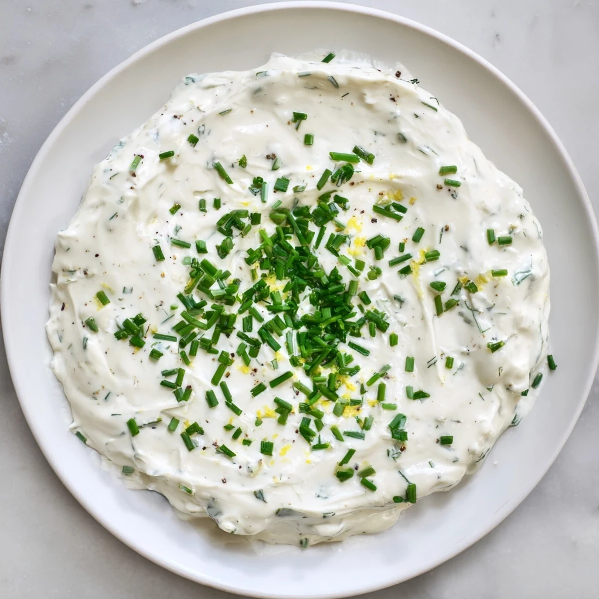 A close-up of Veggie Ranch Dip, showing a thick texture and fresh herbs on top for serving.