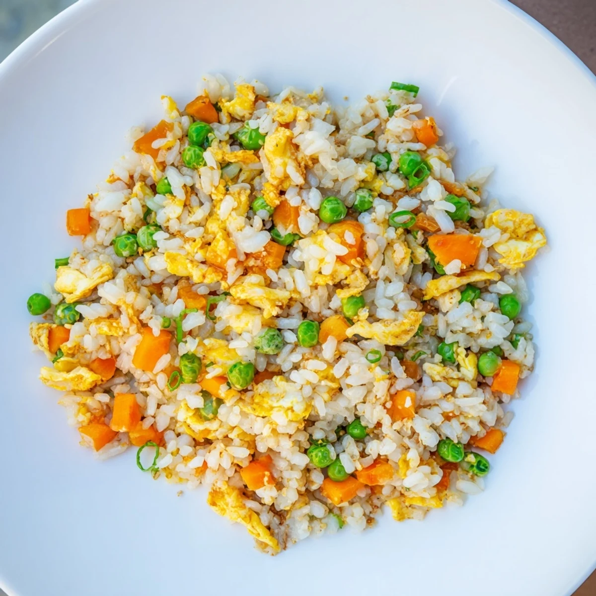 A steaming bowl of egg fried rice with peas and carrots, ready to enjoy at home.