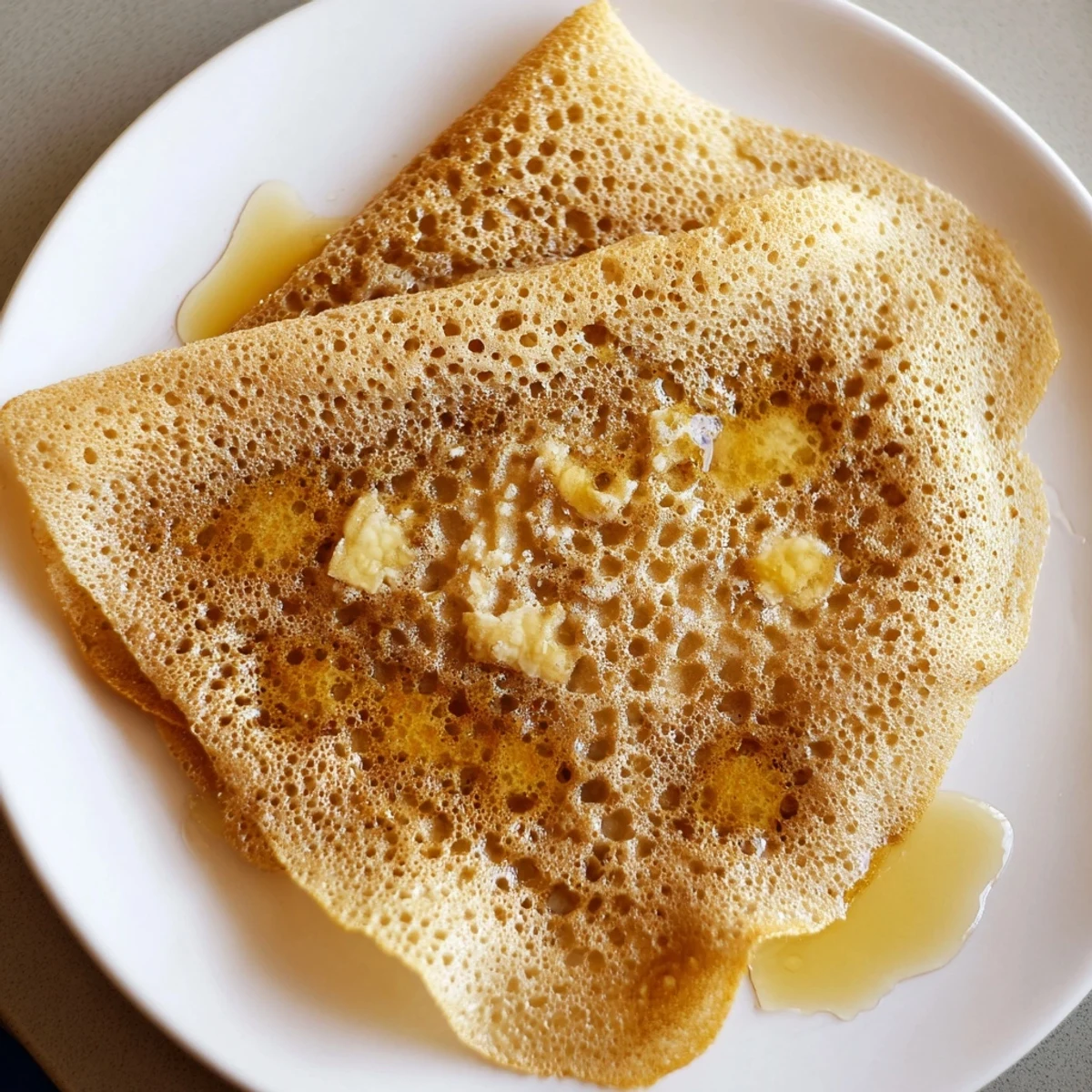 Golden-brown Moroccan Baghrir crepes are bubbling, ready to be soaked with sweet honey butter.