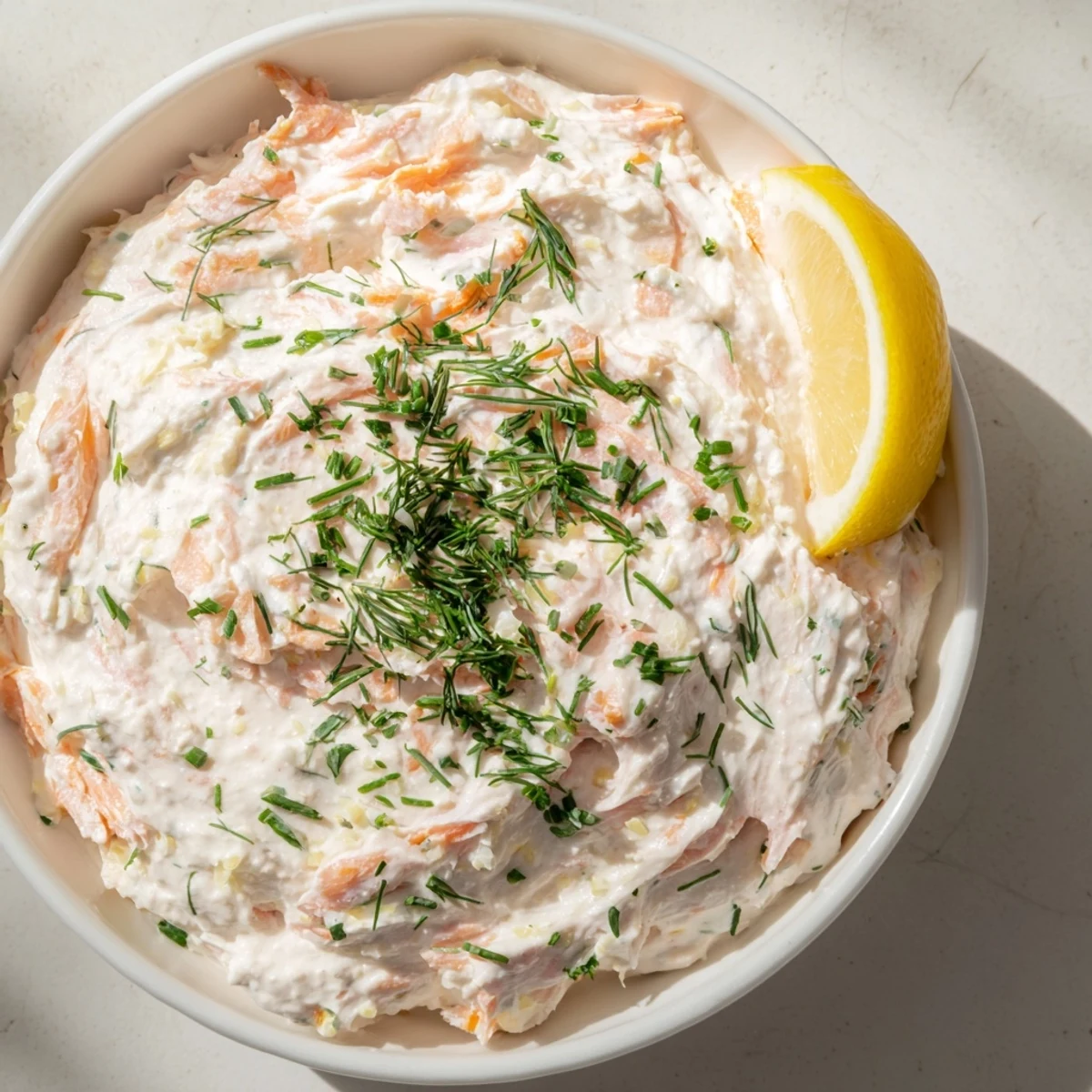 A close-up view of creamy smoked salmon dip garnished with fresh dill and lemon wedges, ready for serving.