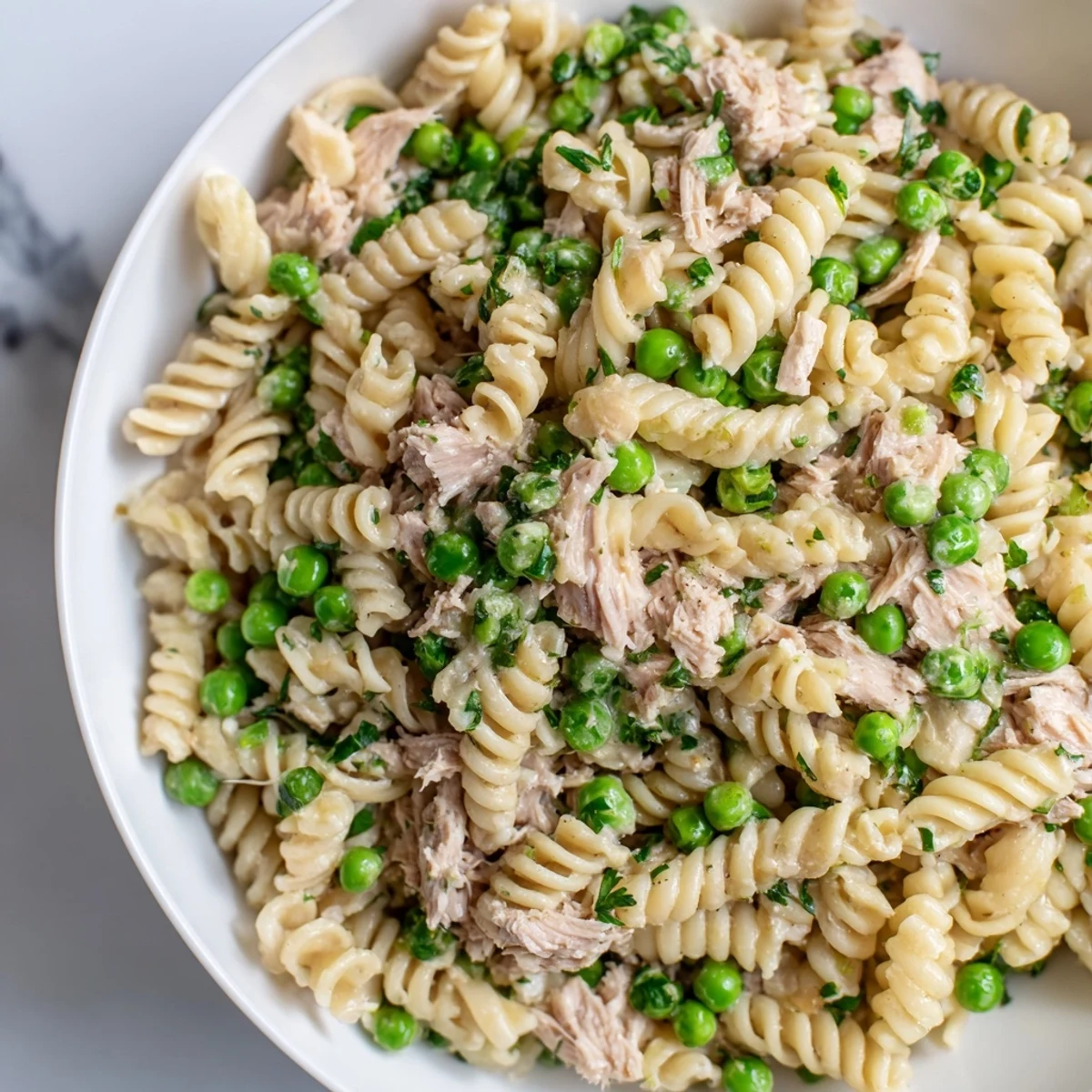 A vibrant bowl of Lemony Tuna Pasta Salad with flaky tuna, bright green peas, and fresh parsley tossed in olive oil.  