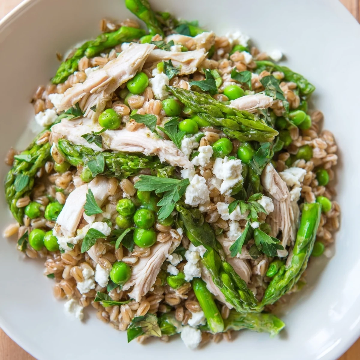 Vibrant bowl of spring farro chicken salad with juicy chicken, blanched veggies, and zesty lemon dressing, served ready to enjoy.