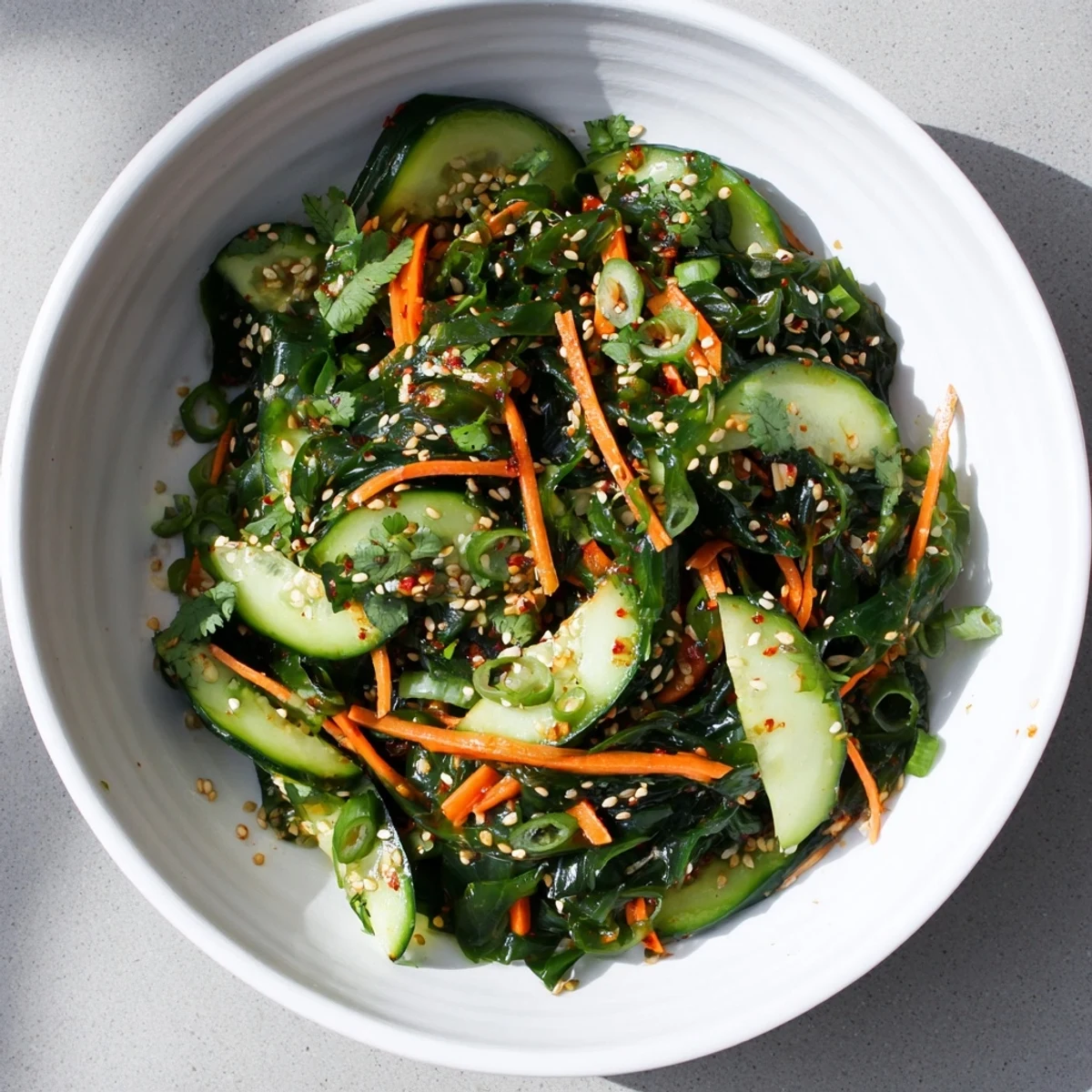 A refreshing Japanese seaweed salad garnished with toasted sesame seeds and fresh cilantro, served in a white ceramic bowl.