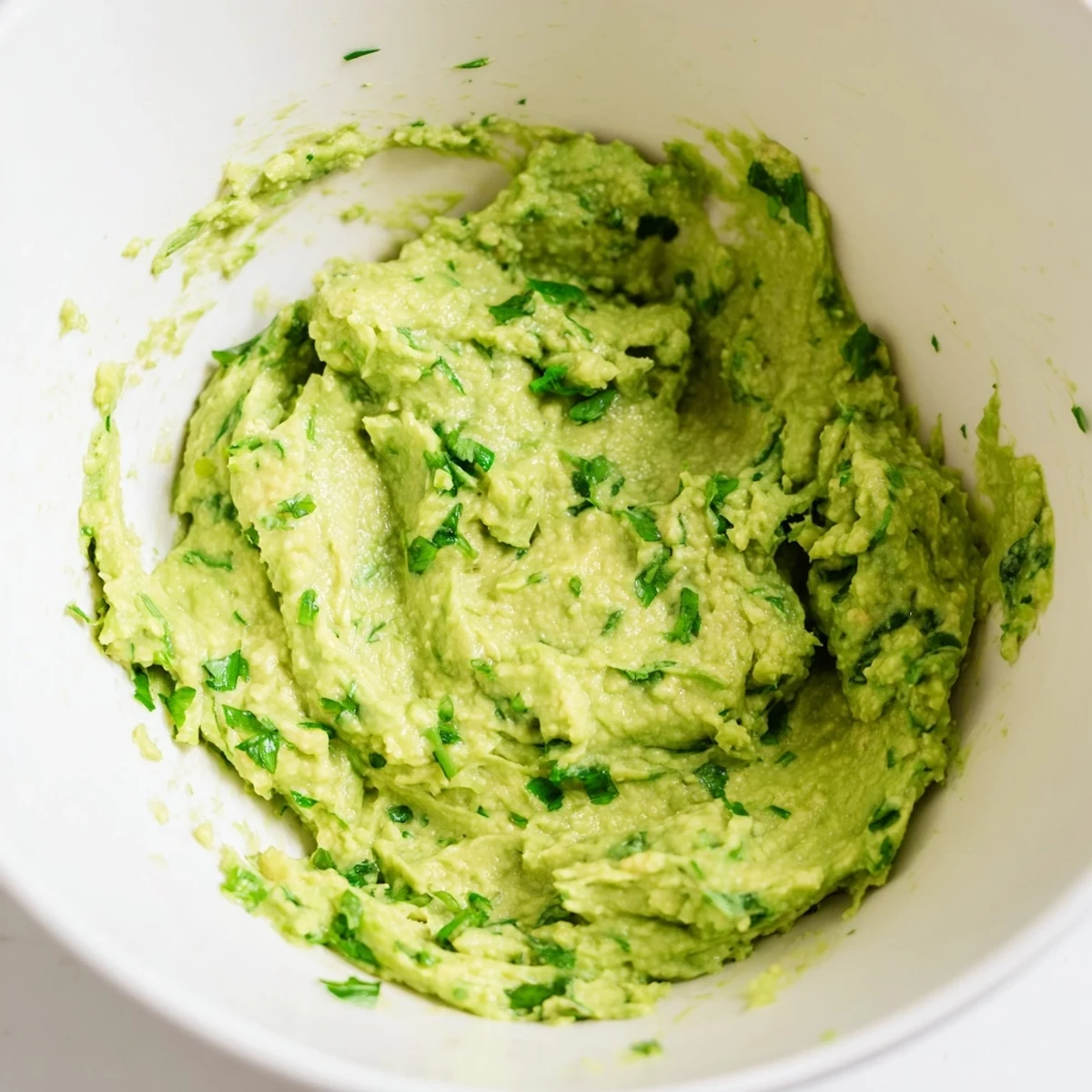 Creamy Avocado Lime Dip in a white bowl garnished with fresh cilantro and lime wedges, ready for dipping.