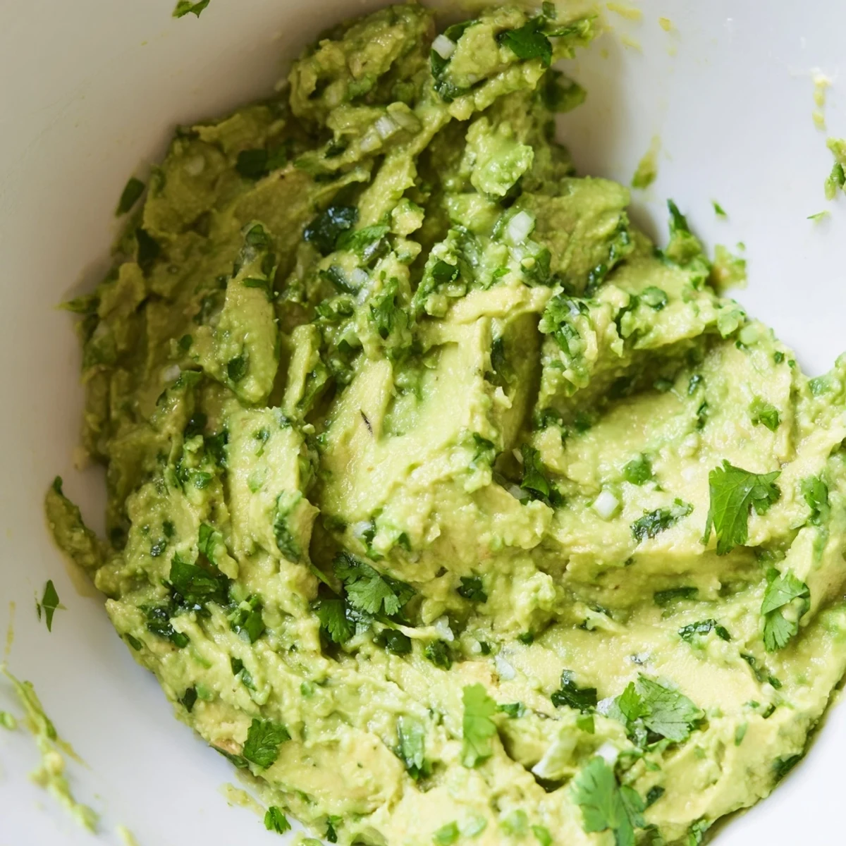 Vibrant avocado dip with garlic and jalapeño surrounded by tortilla chips and crisp vegetable sticks for serving.