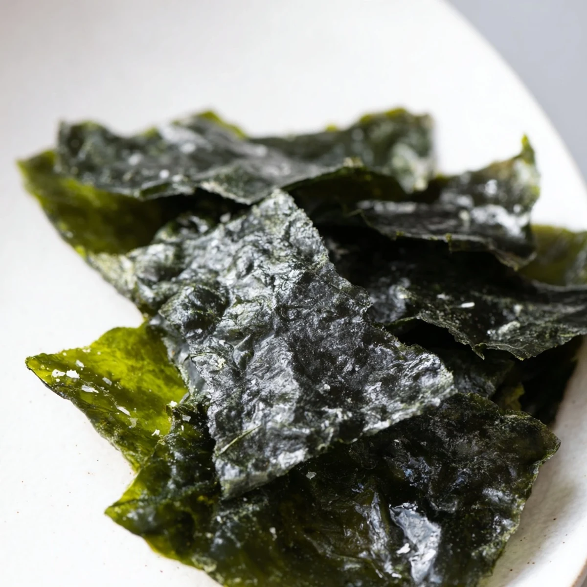 A rustic bowl of roasted seaweed chips garnished with chili flakes, served alongside a rice bowl.