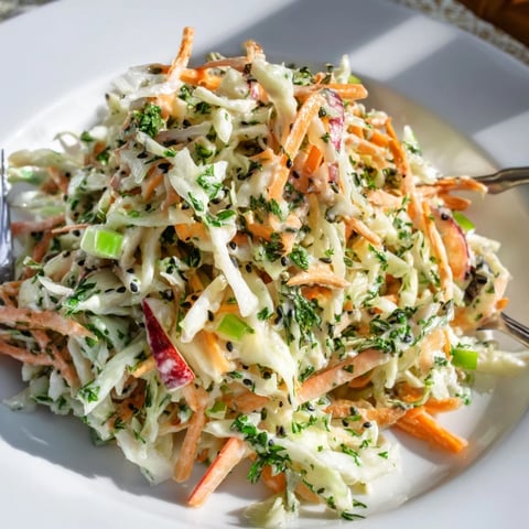 Bright green shredded cabbage, crisp apple matchsticks, and grated carrots tossed in a tangy apple cider vinaigrette, ready to serve.  