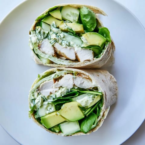 A rolled Green Goddess Wellness Wrap shows the layers of chicken, veggies, and creamy dressing inside.