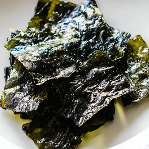 Close-up of crispy, dark green roasted seaweed chips, seasoned with salt and ready to snack.  