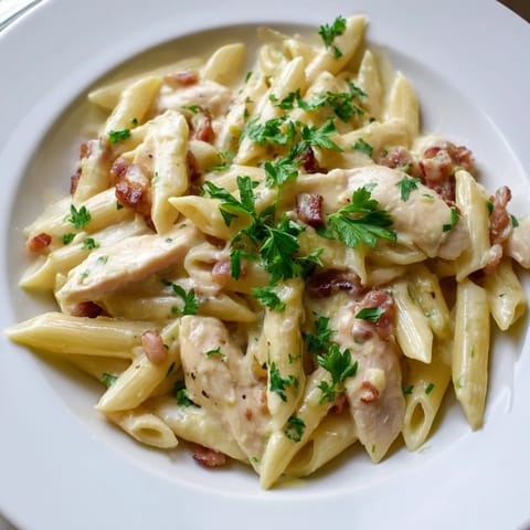 Creamy Chicken Bacon Penne served in a white bowl with steam rising and a side salad for a complete meal.