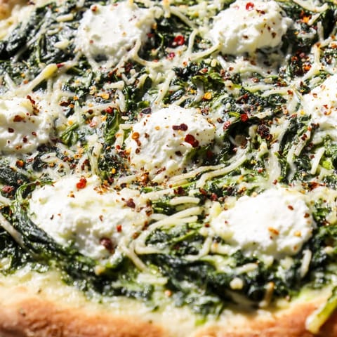 Freshly baked spinach ricotta pizza sliced into wedges, with vibrant green spinach and melted cheese on a rustic table.  