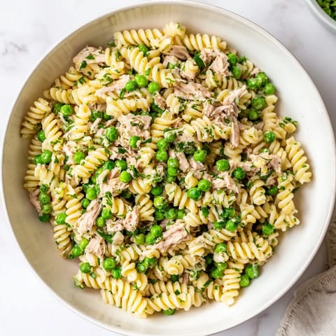Close-up of Lemony Tuna Pasta Salad showing zesty lemon zest, al dente fusilli, and diced red onion glistening in dressing.  