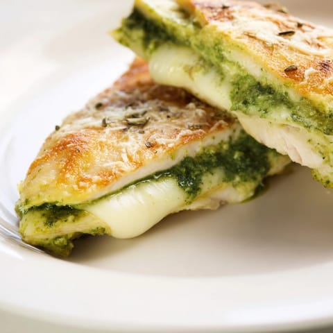 A close-up of a juicy, tender chicken breast slit open to reveal fragrant basil pesto and creamy mozzarella filling.  