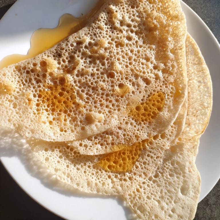 Fluffy and holed, the delicate Moroccan Baghrir is served warm with drizzled honey and melted butter.