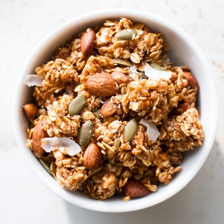 A close-up of Granola Clusters, golden brown clusters with almonds and pepitas, served with milk and fresh berries.