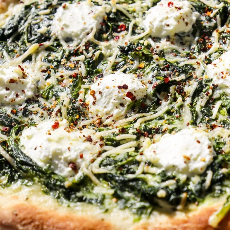 Freshly baked spinach ricotta pizza sliced into wedges, with vibrant green spinach and melted cheese on a rustic table.  