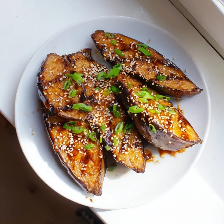 Close-up of silky miso glazed eggplant with a glossy glaze, toasted sesame seeds, and fresh green onion garnish.